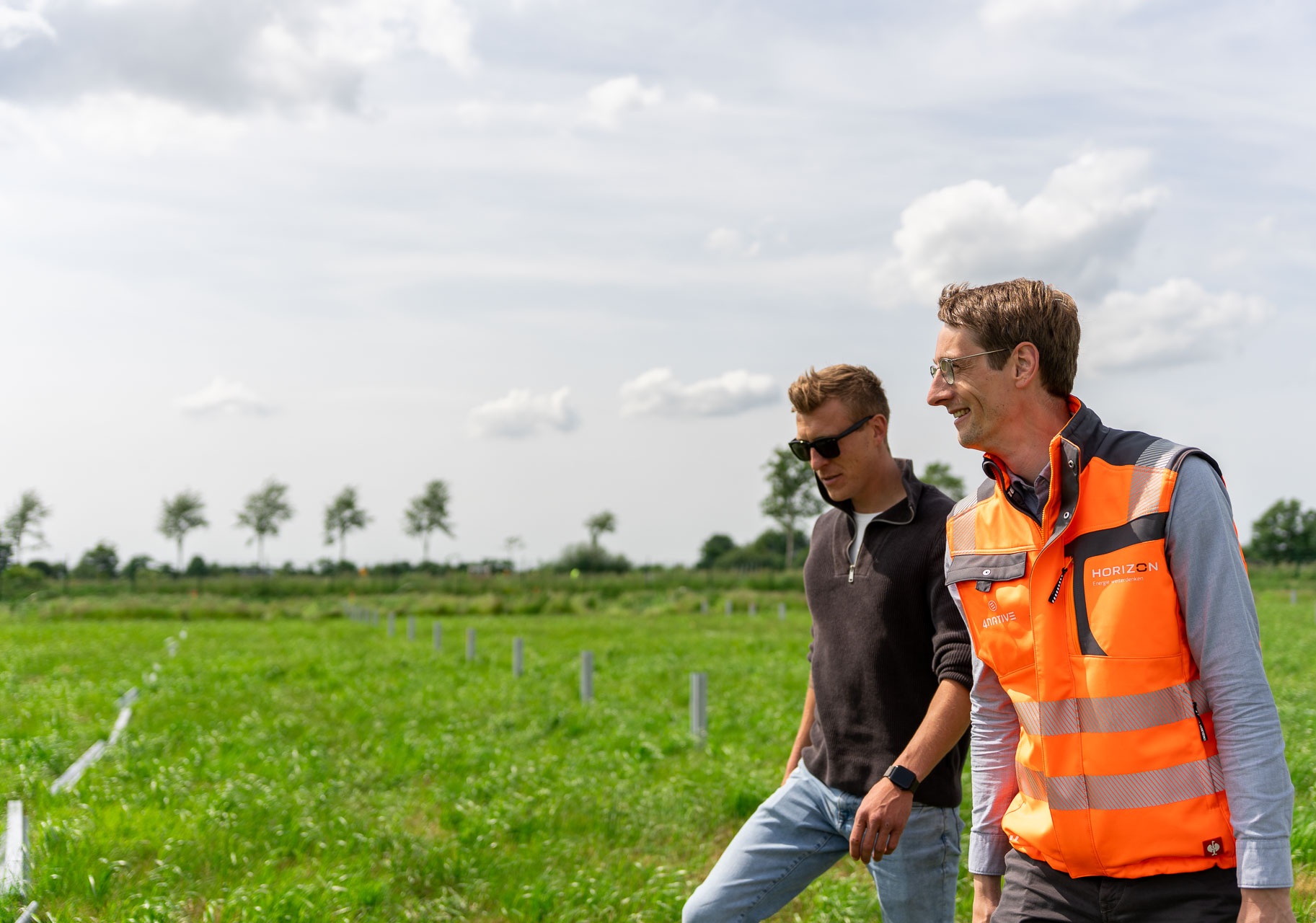 HORIZON-Geschäftsführer Melf Jensen und Thomas Kals gehen nebeneinander über eine Wiese, auf der eine PV-Freiflächenanlage gebaut wird.