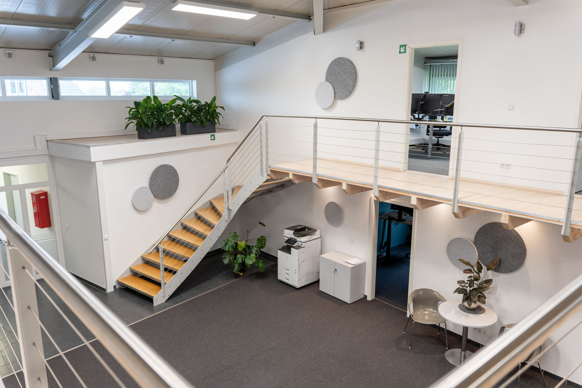 Das Büro hat weiße Wände, einen dunkelgrauen Boden, minimalistische Deko, Grünpflanzen und sanfte Beleuchtung. Es wirkt freundlich.