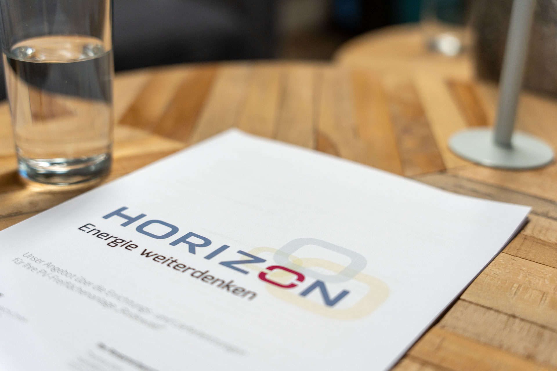 Nahaufnahme von einem HORIZON-Flyer mit großem HORIZON-Logo. Der Flyer liegt auf einem Holztisch.