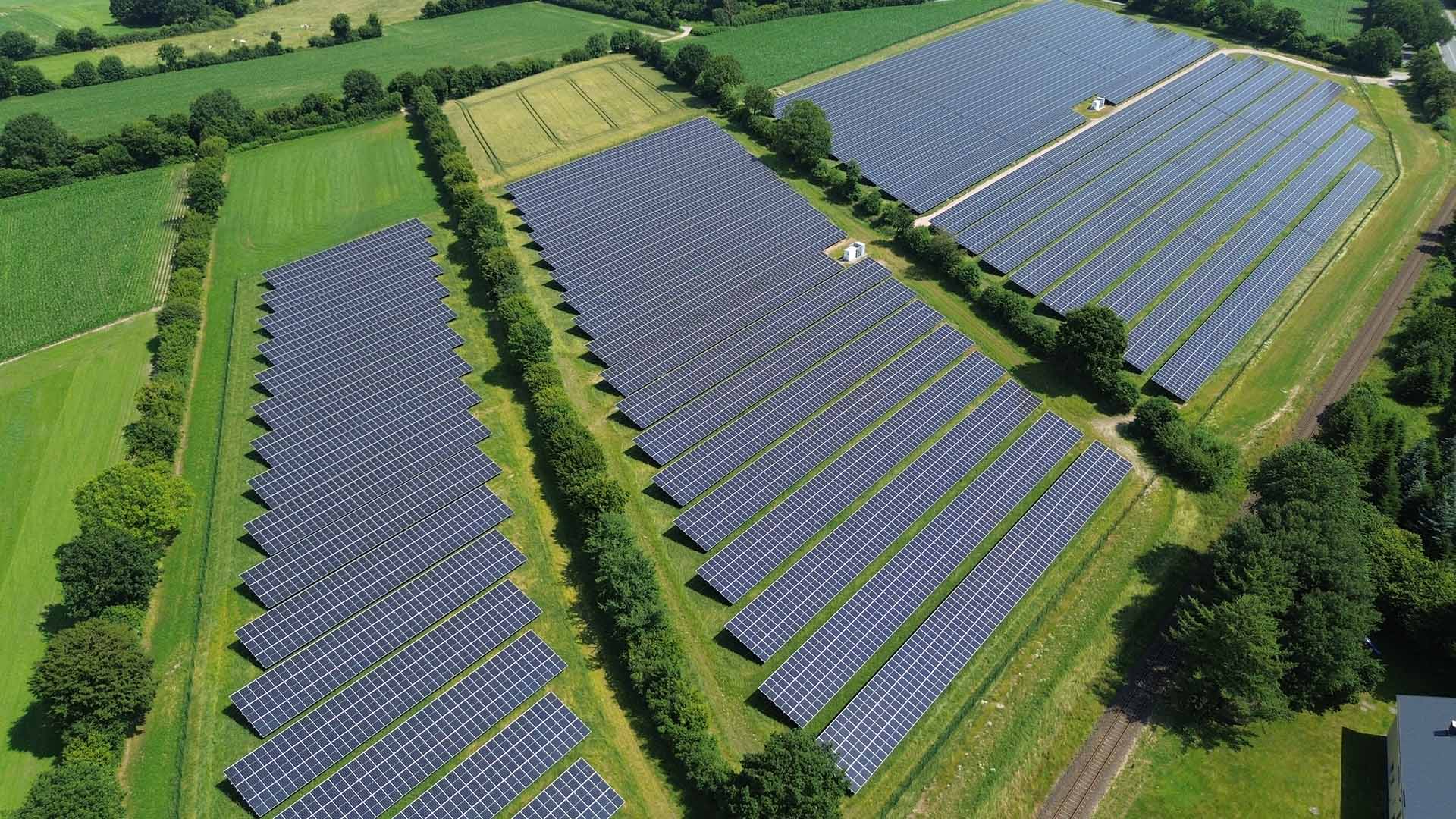 Aus der Vogelperspektive: Eine PV-Freiflächenanlage inmitten grüner Felder und Knicks.
